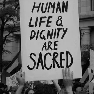 black and white photo of a protest sign being held up that says "human life and dignity are sacred"